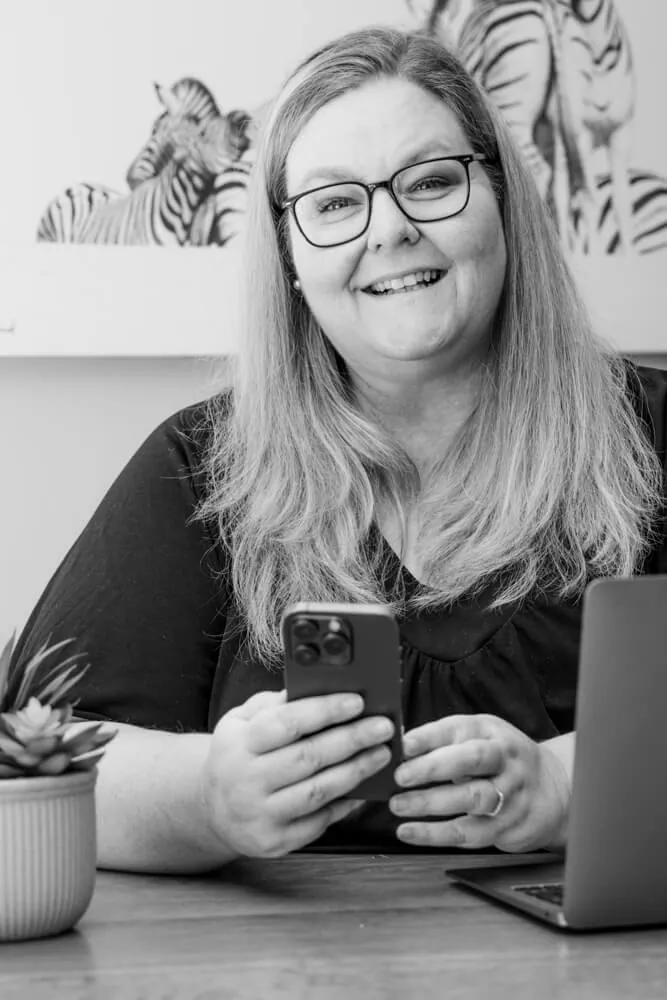 Petro Stroud smiling at her desk with her phone and laptop