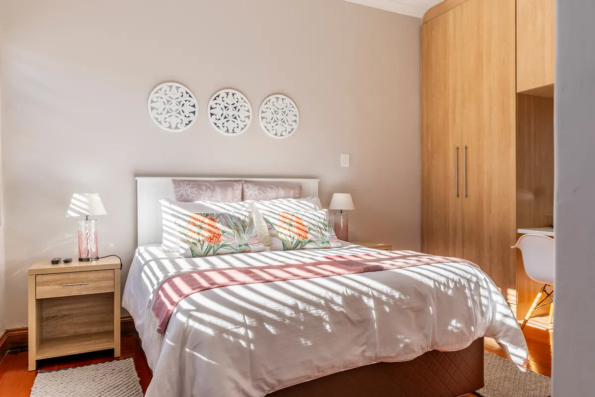 A sunlit guest bedroom with a double bed, bedside lamps and a wooden wardrobe