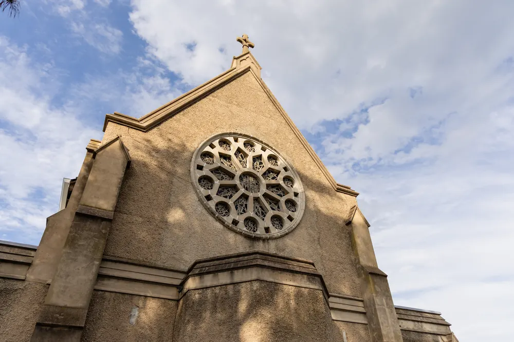 A sandstone church gable with a round rose window against a cloudy sky