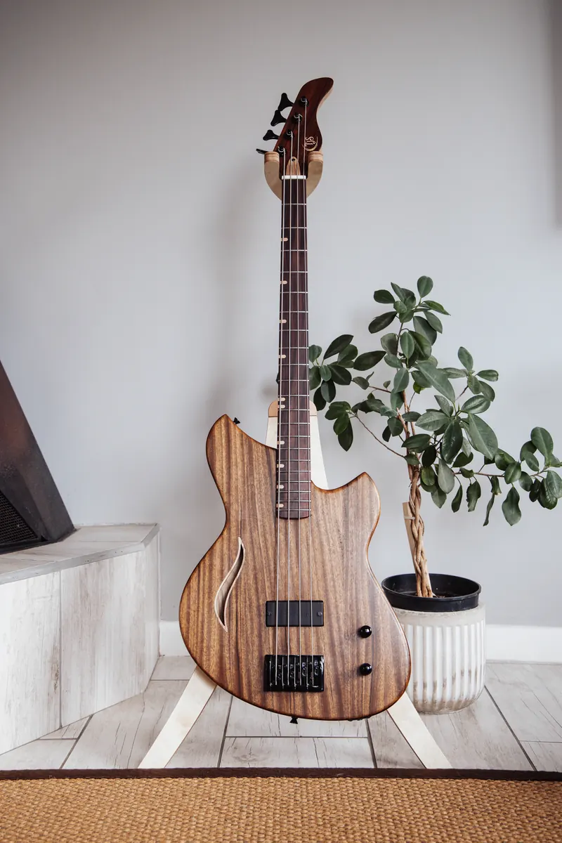 A handmade wooden bass guitar on a stand beside a potted plant