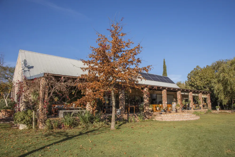 A stone and brick country venue with a wide veranda, lawn and autumn tree